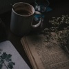 thelaughingmuse: Two open books on a dimly-lit tabletop, with a large mug higher up the table, at the upper edge of the picture. (Books and warm drinks - perfection)